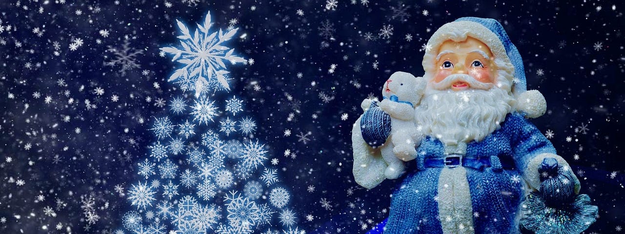 Santa figurine in blue, holding a white baby bear and a small bag of gifts. A Christmas tree made of snow flakes is on its left.