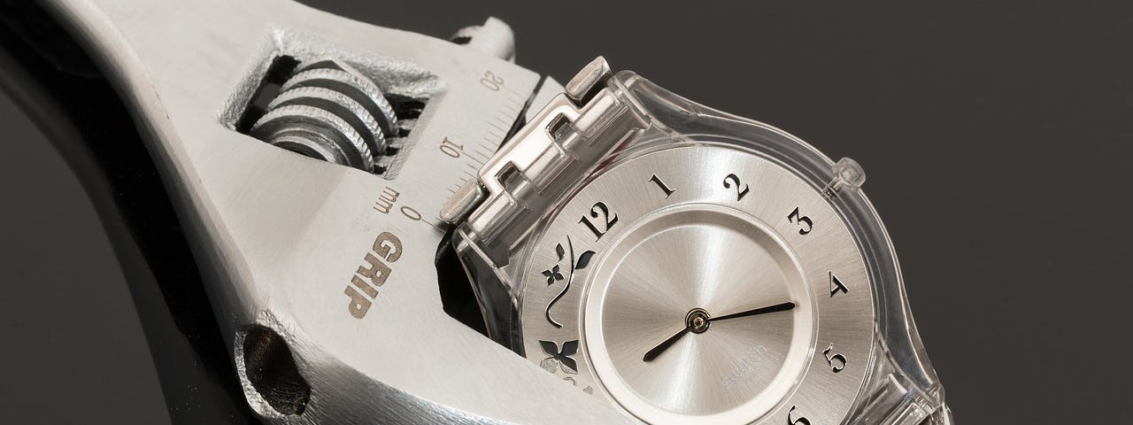 A Spammer Tool Positioned On A Silver Wristwatch Against A Grey Backdrop.