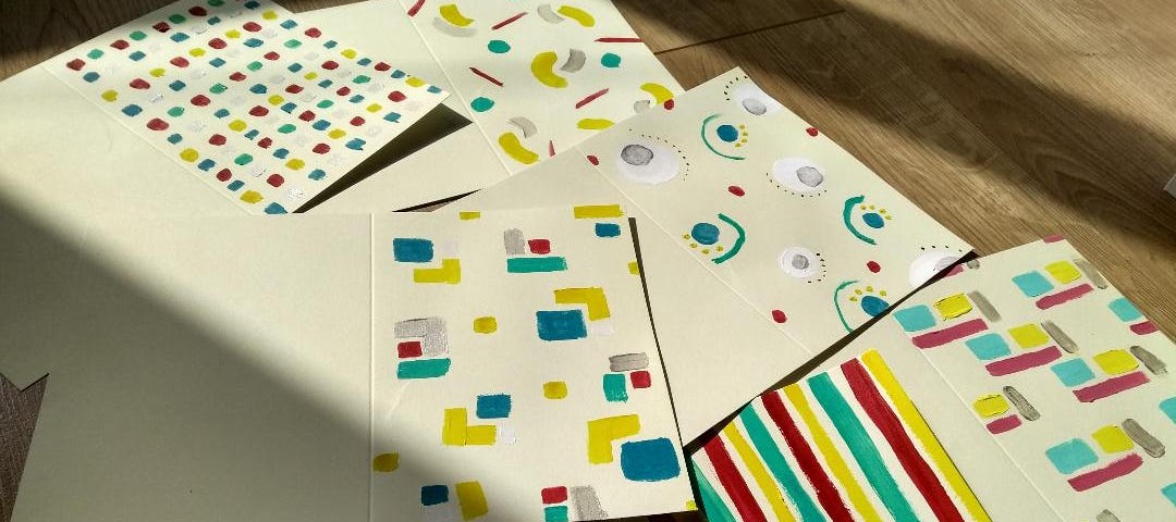 Unfolded cards laid out on the floor, each with colourful painted patterns in yellow, green, red, blue and silver.