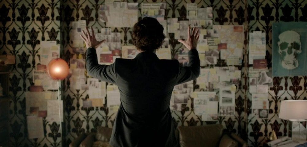 Sherlock Holmes throws his hands up in victory as he solves the case be examining his ‘crazy wall.’