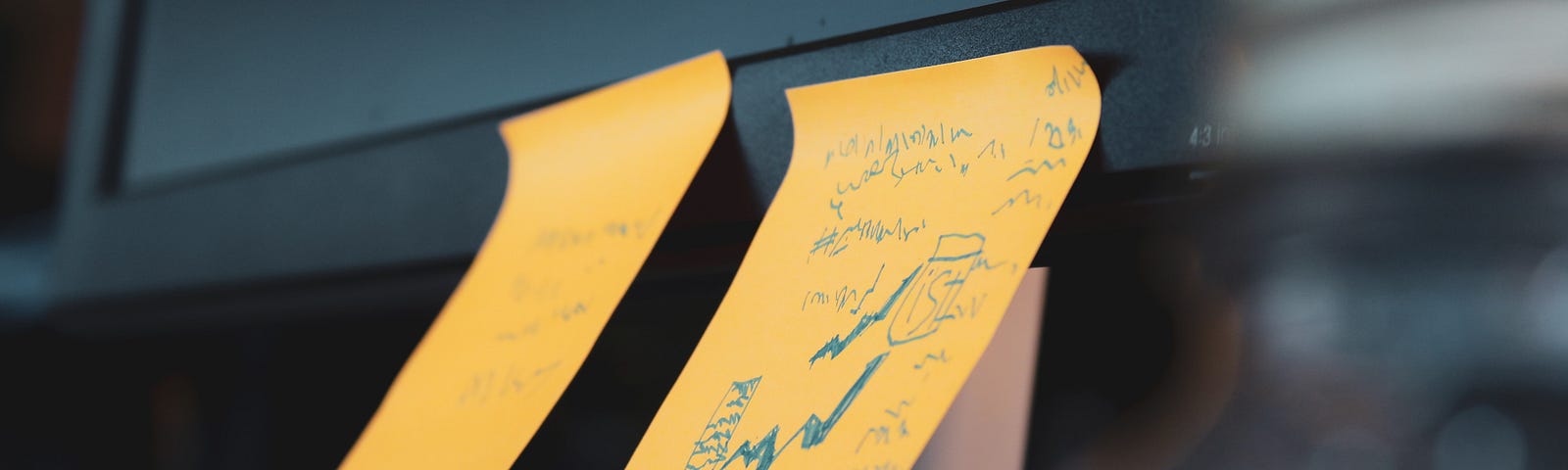 Two orange post-its with blue scribbling stuck to a computer screen.