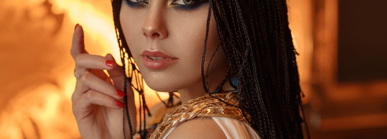 Image of young woman dressed in a white robe with gold jewellery / accessories, dark long hair in braids, Egyptian themed costume