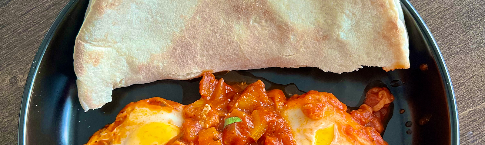 Shakshuka dish pictured on a table with pita bread