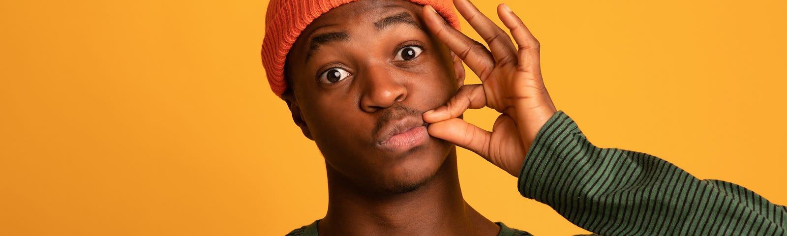 A man in an orange hat makes the sign of “zipping his lips” against a yellow background.