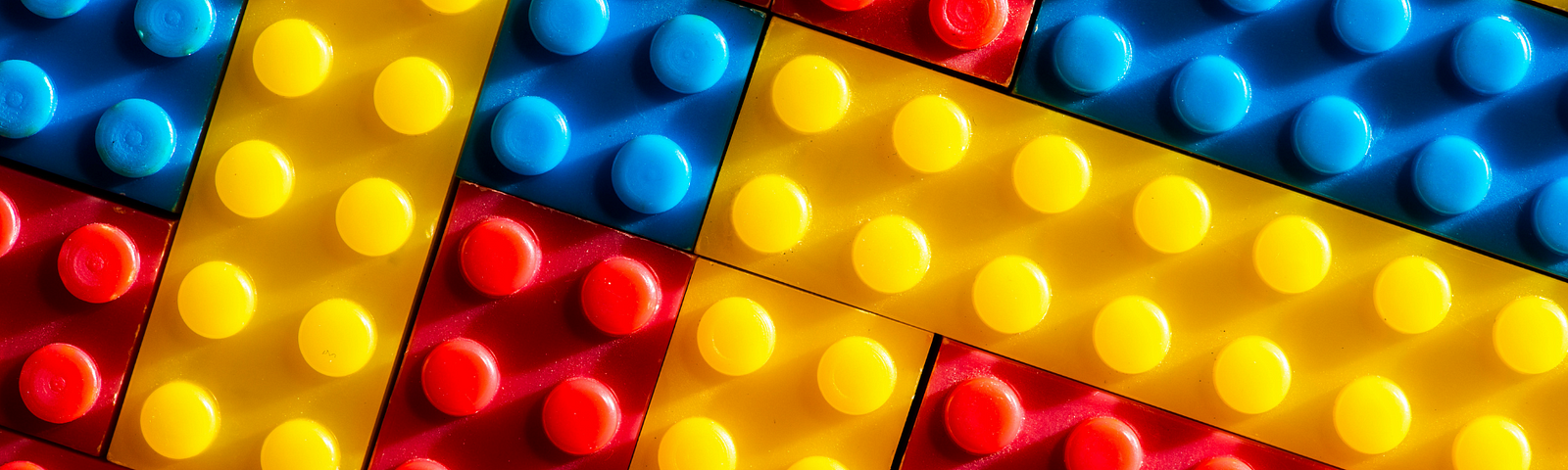 Blocos de lego azuis, amarelos e vermelhos organizados um ao lado do outro em diagonal.