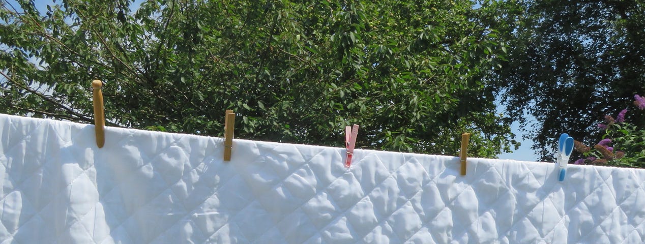 Quilted bed sheet with various types of pegs holding it to a washing line.