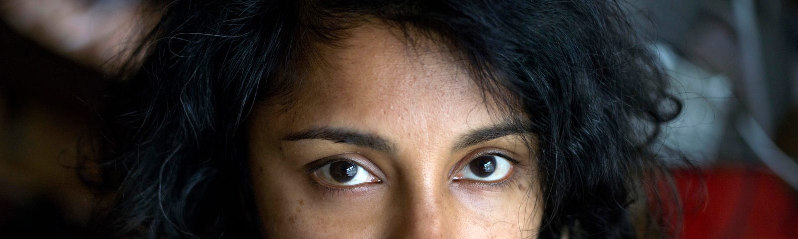 Headshot of author Devika Ponnambalam, with dark wavy hair and black blouse looking at the camera, credit Graham Clark