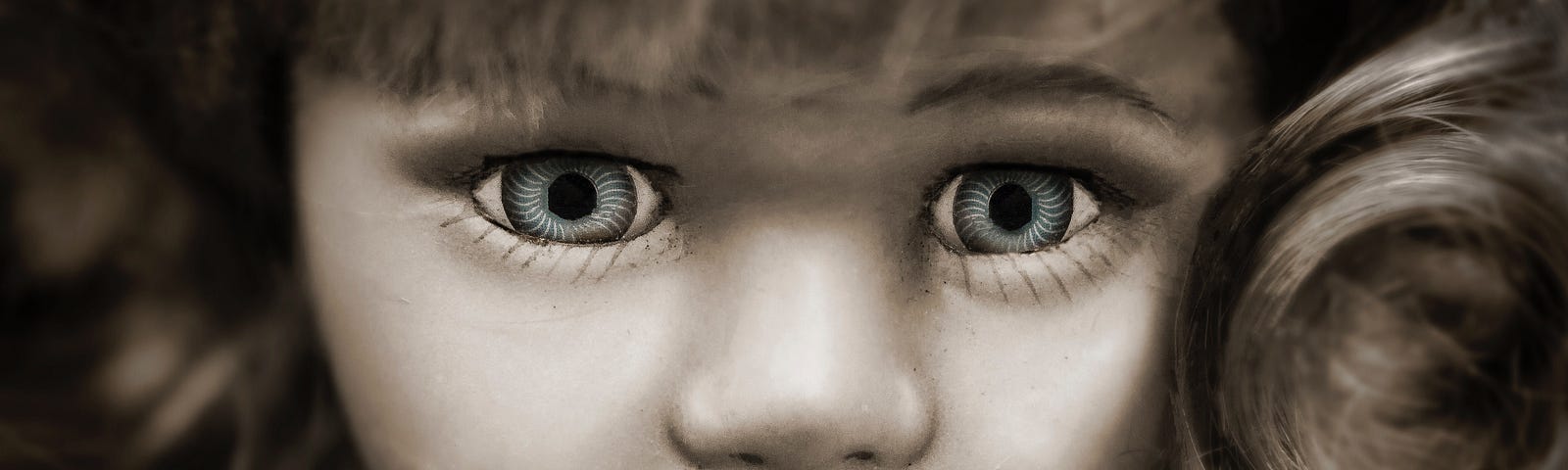 An image of a porcelain doll face with piercing blue eyes and blond wavy hair softly framing her face.