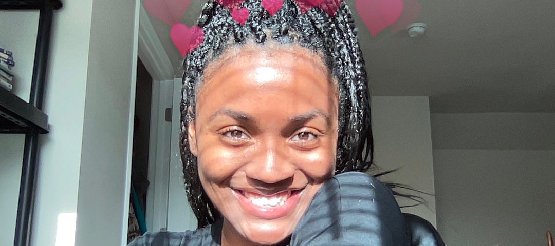 A fine ass Black woman smiles into the camera; with a halo of hearts around her head.