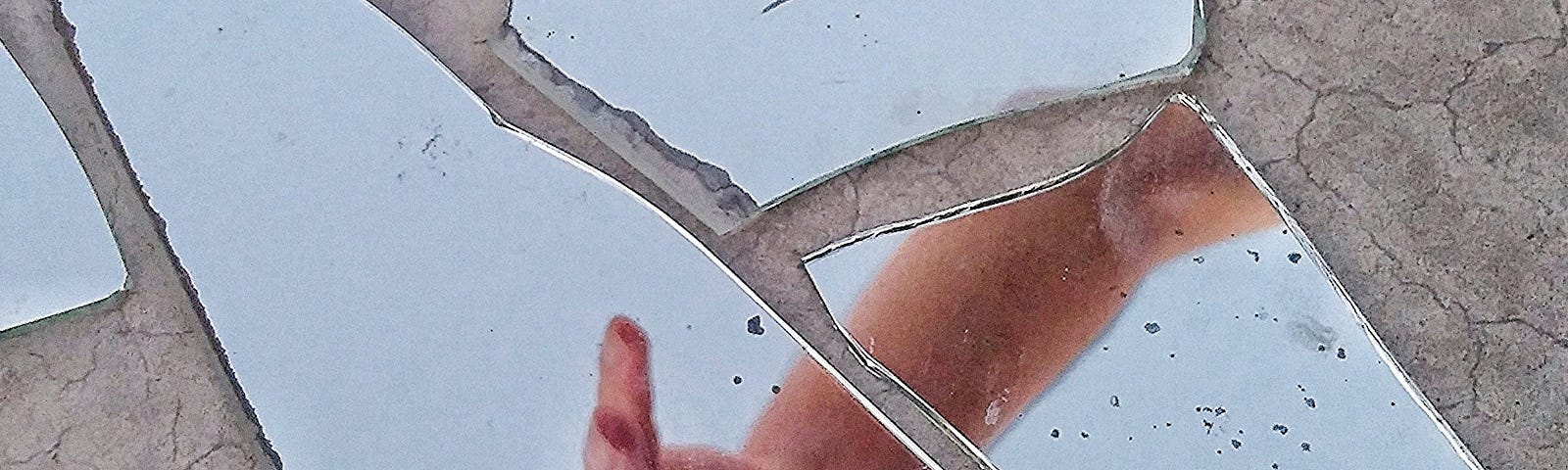 Mirror Fragments on Gray Surface With The Reflection Of A Person’s Hand