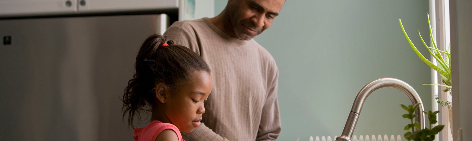 Father and daughter wash hands together at the kitchen sink.