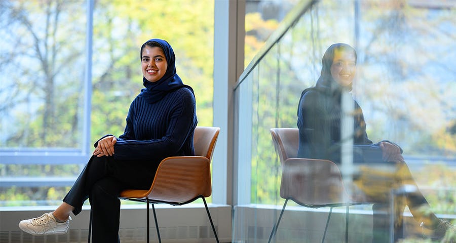 Sarah Alnegheimish sits in front of a wall of windows overlooking out-of-focus trees.