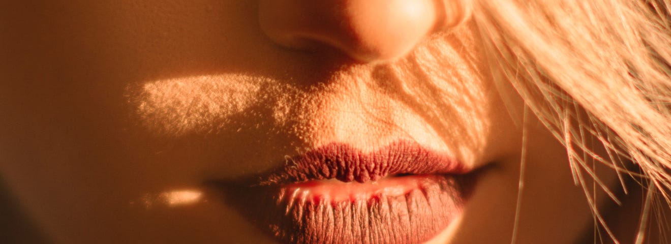 A close-up of a blonde woman’s lower face. Her lipstick is dark red.