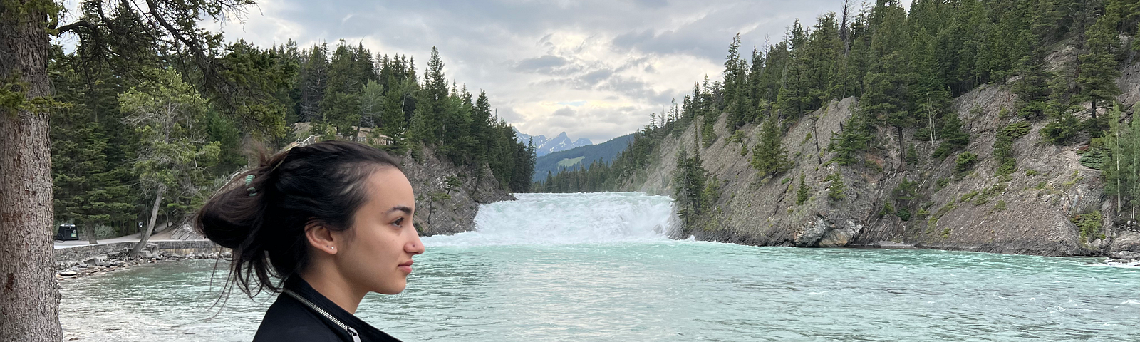 Photo of author in a black zippered jacket looking out at a river in the Canadian rockies.