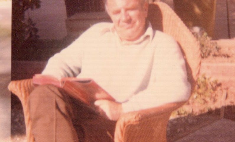 A middle-aged man sits reading in the sun.