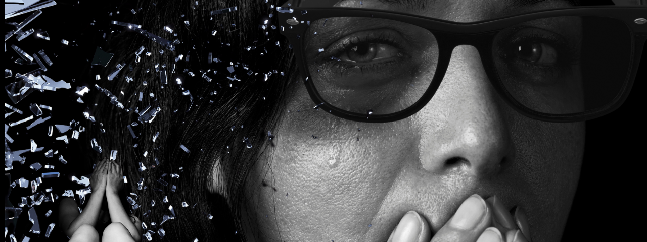 women with slight bruise near eye with tear over it hidden under dark sunglasses. In the corner under shattered glass a woman sits hiding her face.