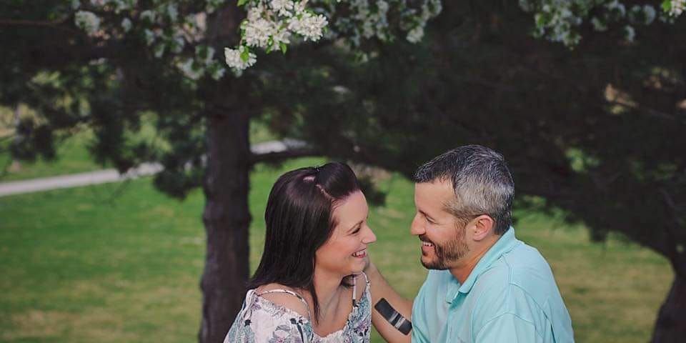 Shanann and Chris Watts sitting in a park smiling at each other.