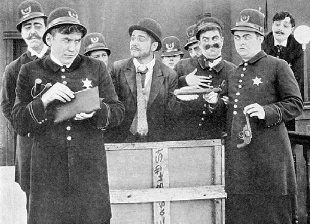black and white photo of several keystone cops surrounding a witness in court