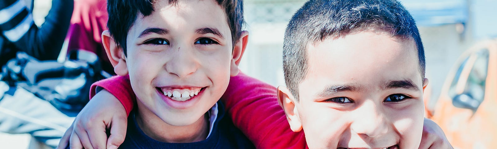Two young boys smiling at the camera with arms around each other’s shoulders