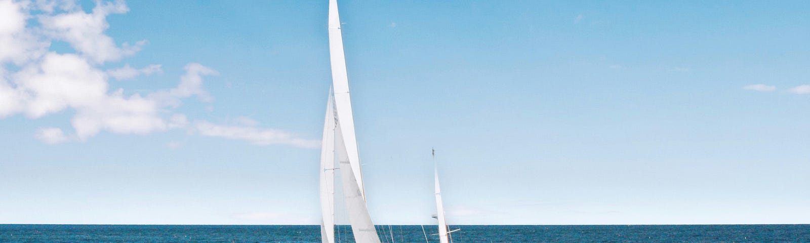 Blue ocean with sailboat with white clouds on left side of blue sky.