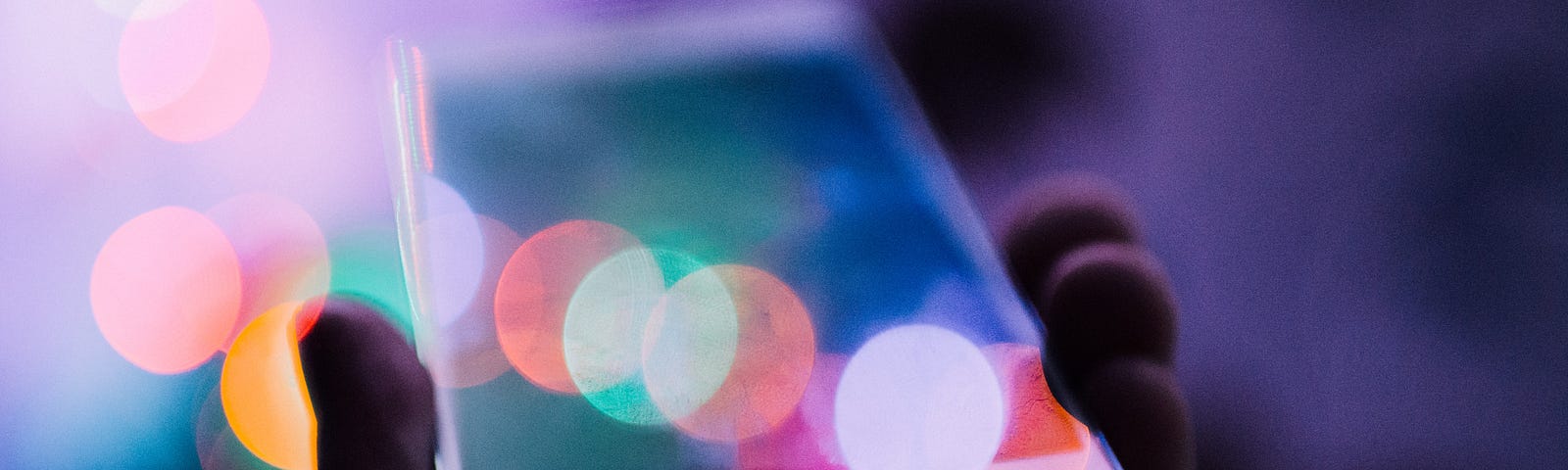 A person holding a phone in their hand with lights blurring across the screen and into the distance of an out-of-focus background