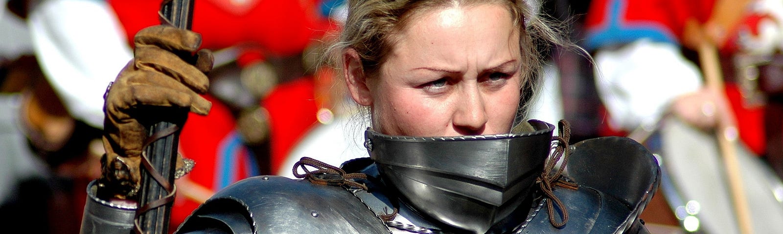 A woman wearing heavy plate armour, her head bare.