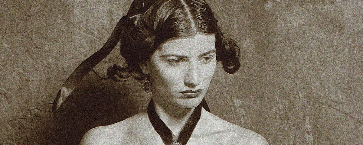 A black and white image of a sombre woman in an off-the-shoulder Edwardian dress. She is not looking directly at the camera.