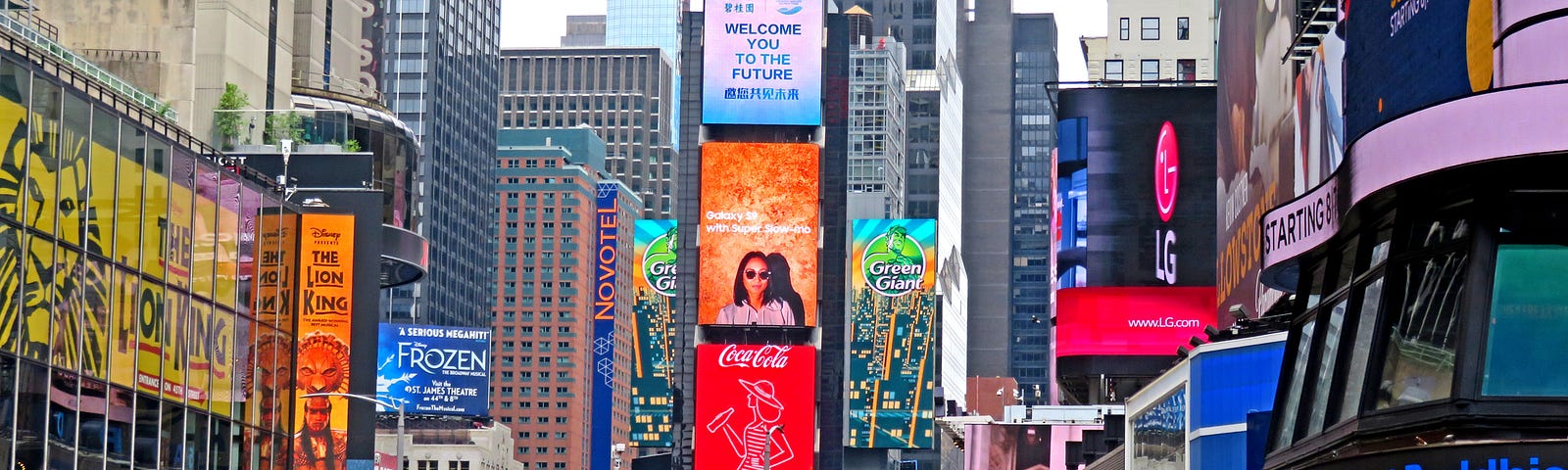 camera shot is looking over the heads of a large crowd of people on the pedestrian zone at Times Square. There are colorful billboards and signage all around.