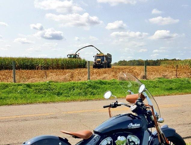 Black Indian Scout motorcycle sitting on a country road beside a field where harvest is taking place.