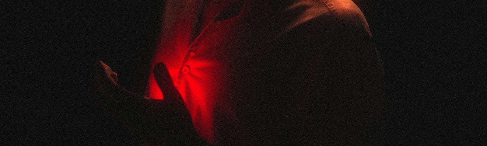 A red glow against a person’s chest, tehir hand held close to their chest