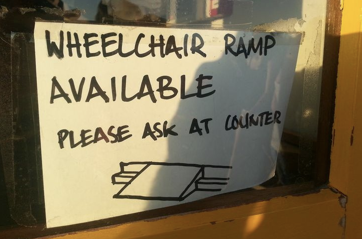 Hand-written sign in a store window reads: wheelchair ramp available please ask at counter