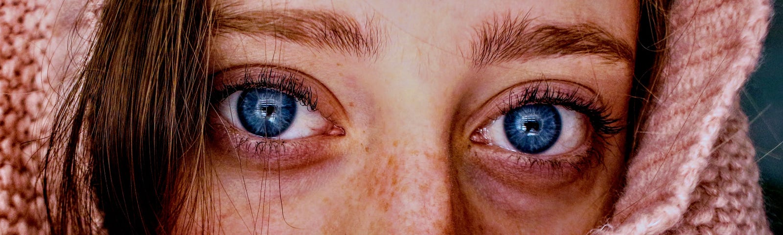 blue eyes of a woman wearing a pink sweater that wraps around her face