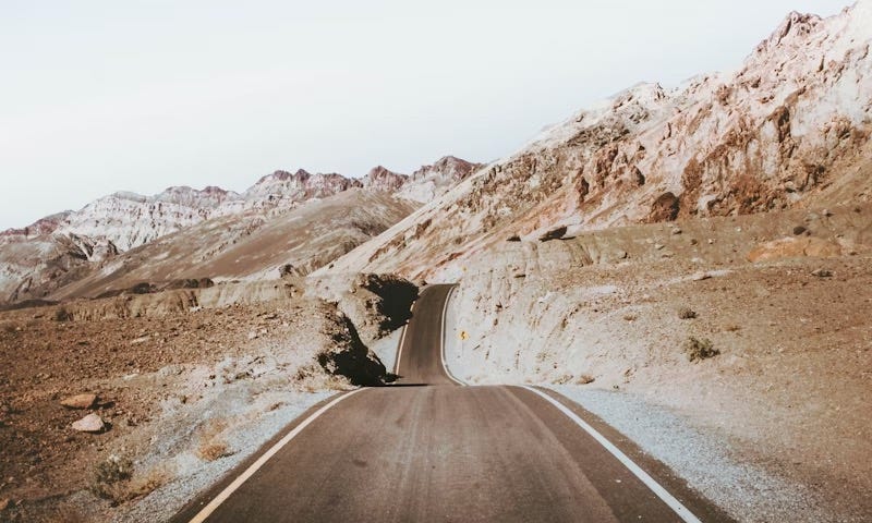 Sepia image of a road running through a barren, but hilly, landscape towards some distant mountains