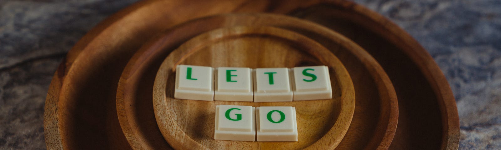 Blocks of letters that spell out “LETS GO” on three wooden plates.