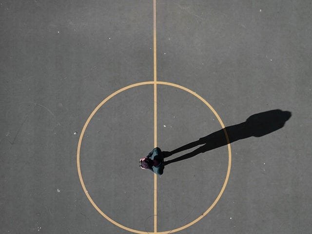 Image from above of a man standing in the middle of the centre circle of an asphalt basketball court