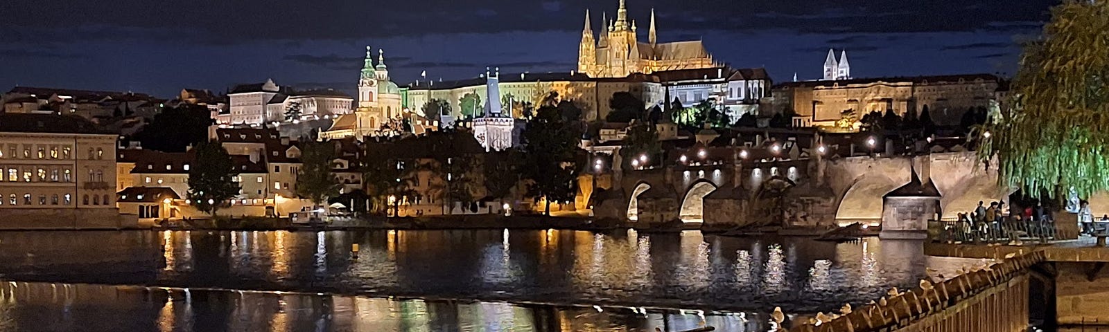 A view of a river and a bridge with a background of a castle lit with lights in the night.