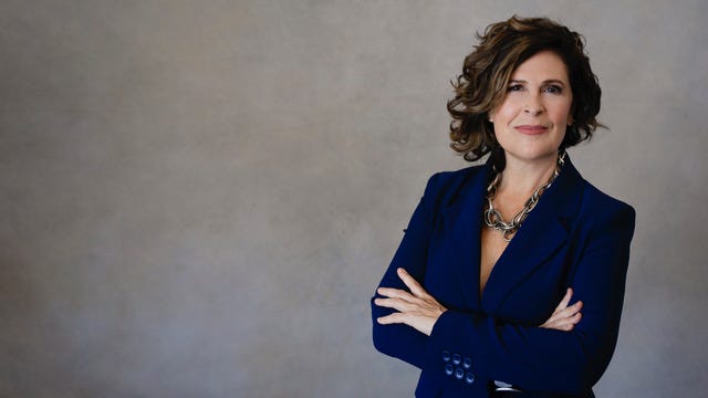 Susan Harrow in a navy blazer with arms crossed against a grey background