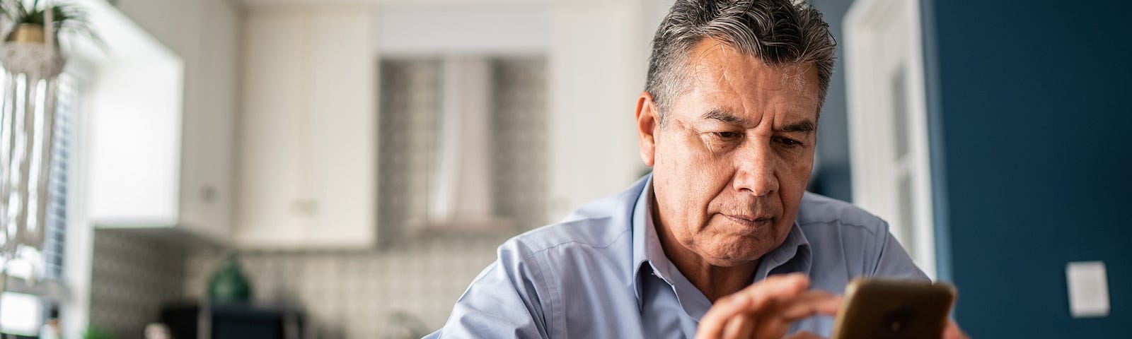 Older man with gray hair sits at table using phone