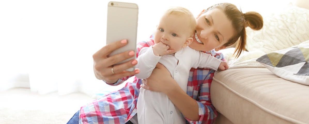 Mother holding a baby and taking a photo of them both.