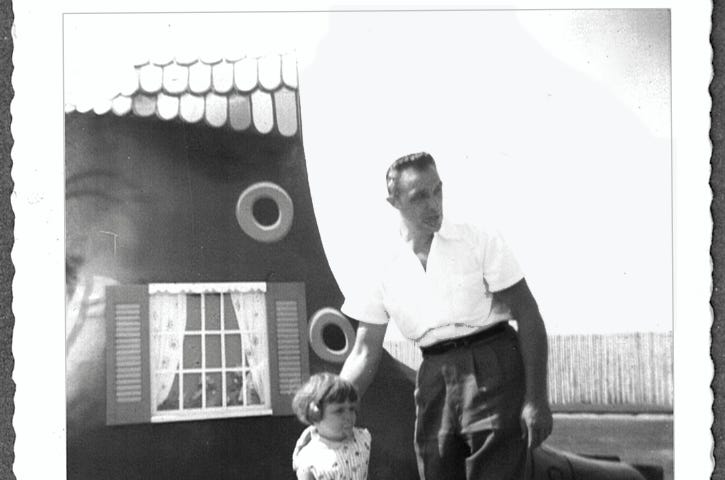My Dad with his arm on my shoulder, standing in front of a giant shoe at a theme park, circa 1960.