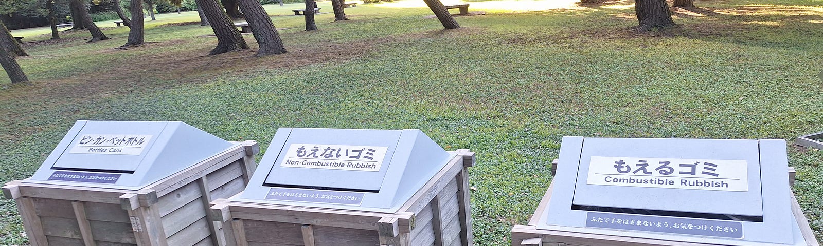 Three wooden rubbish box containers in a Tokyo park, Japan. Labelled bottles/cans, non-combustible and combustible, in Japanese and English.