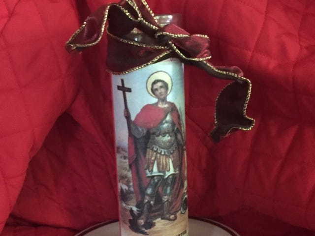 A photo of a tall votive candle portraying a Roman Centurion holding a cross in one hand and a palm frond in the other. Saint Expedite.