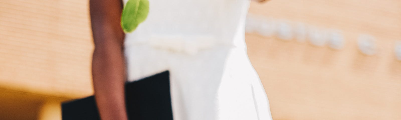 A woman in a white dress throws a rose at the camera. The flower is in focus, but she is not. She holds a diploma in her right hand.