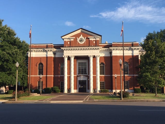 Red brick courthouse with two-story white pillars sits in the center of a typical small town square.