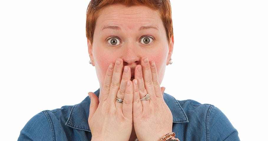 Woman with shocked face, eyes wide and hands covering mouth.