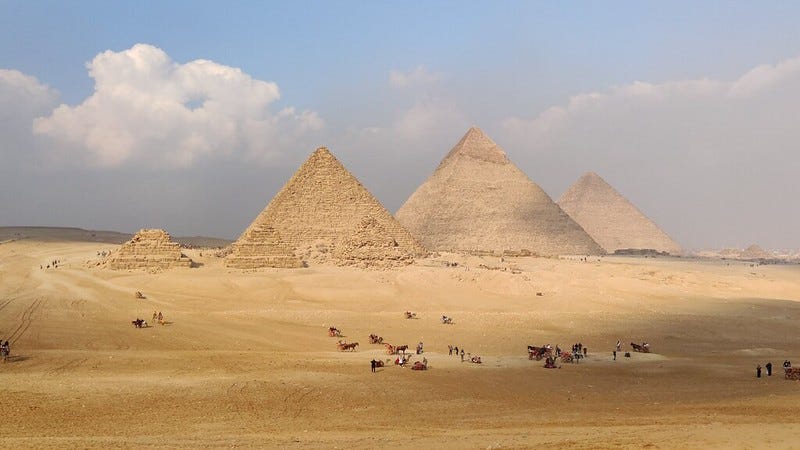 The great pyramids of Giza, Egypt, with desert in front and a blue sky with clouds behind.