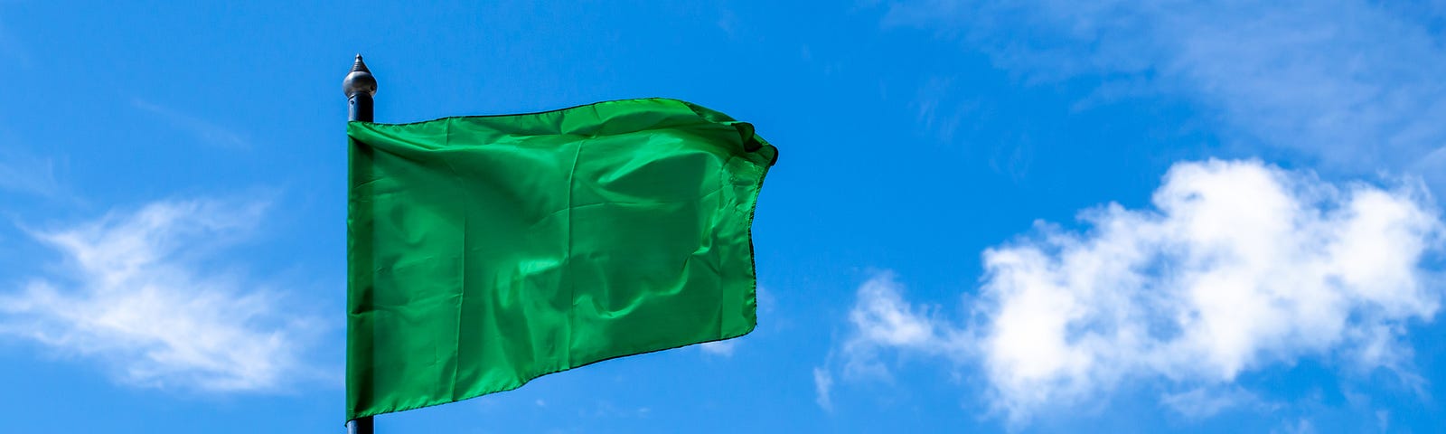 A large green flag flying at the top of a flagpole, against a blue sky.