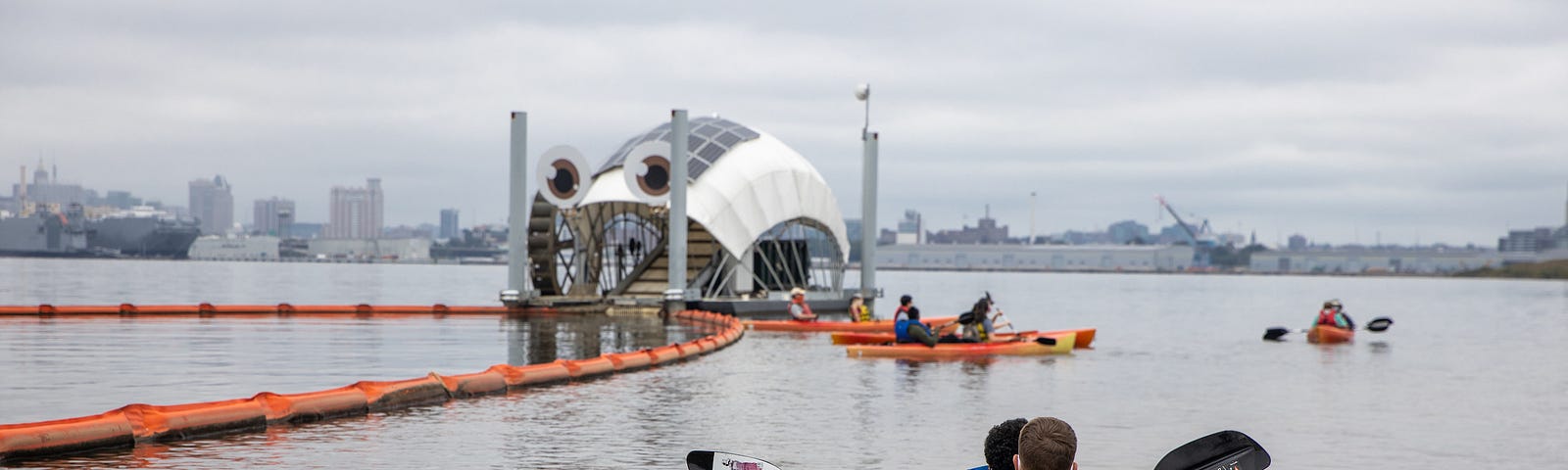 a two person kayak paddles towards a floating structure with eyes and more boaters