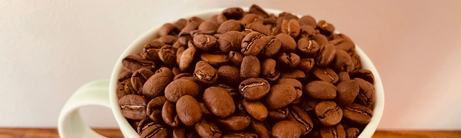 A coffee cup full of coffee beans sits on a stained oak shelf.