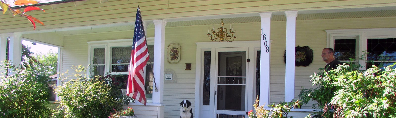 Old house with flag flying, dog on porch